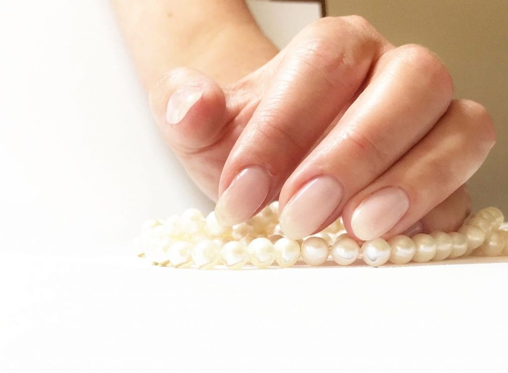 A zoomed in image of a persons hand with a pearl necklace